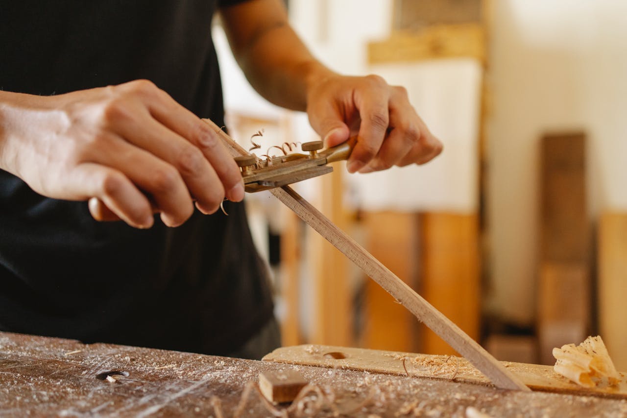 Faceless man planing thin plank with manual tool at workbench in modern light studio